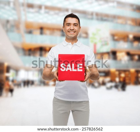 shopping, consumerism, discount and people concept - smiling man with red sale sign over mall background