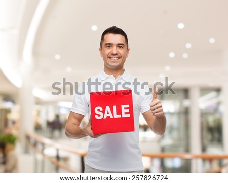 shopping, discount, consumerism, gesture and people concept - smiling man with red sale sigh showing thumbs up over mall background