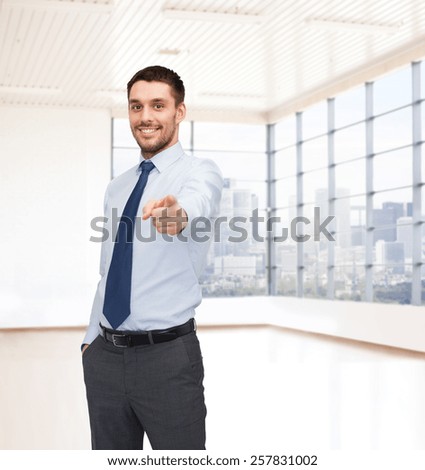 business, people and office concept - happy young businessman pointing finger at you over office room or new apartment background