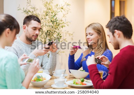 people, leisure, friendship and technology concept - group of happy friends with smartphones taking picture of food at cafe