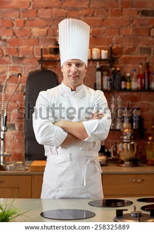 cooking and people concept - happy male chef cook with crossed hands in restaurant kitchen