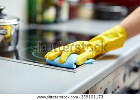 people, housework and housekeeping concept - close up of woman hand in protective glove with rag cleaning cooker at home kitchen