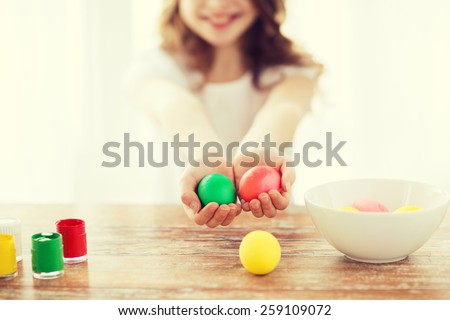 easter, holiday and child concept - close up of little girl holding colored eggs with colors and bowl on the table
