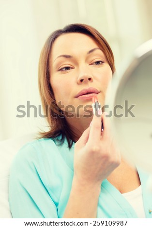 cosmetics and beauty concept - beautiful woman applying lipstick and holding mirror