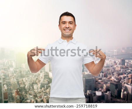 happiness, advertisement, fashion, gesture and people concept - smiling man in t-shirt pointing fingers on himself over city background