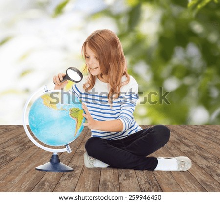 education, travel, childhood, geography and school concept - happy little student girl looking at globe with magnifier over green background