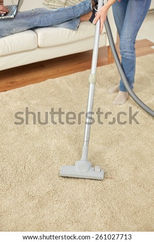 people, housework and housekeeping concept - close up of couple legs and vacuum cleaner on carpet at home