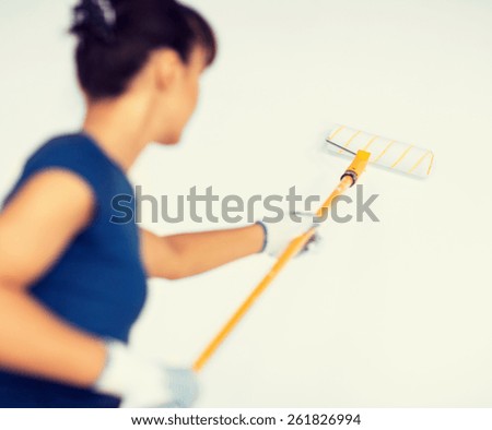 interior design and home renovation concept - woman with roller and paint colouring the wall