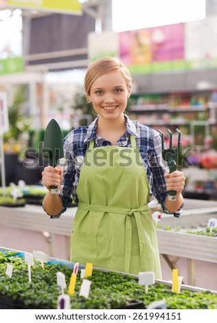 people, gardening tools and profession concept - happy woman or gardener with trowel and fork in greenhouse