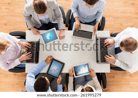 business, people and technology concept - close up of creative team with laptop and tablet pc computers displaying charts on screens sitting at table in office