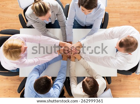 business, people, cooperation and team work concept - close up of creative team sitting at table and holding hands on top of each other in office