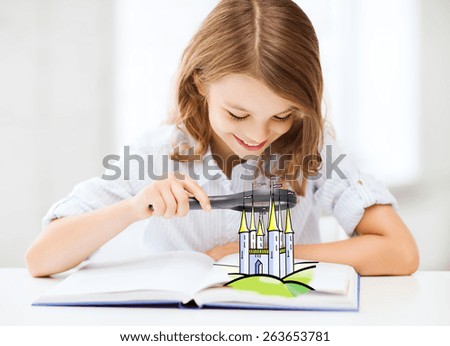people, childhood, literature and imagination concept - little girl with book looking to fairy castle through magnifier at home