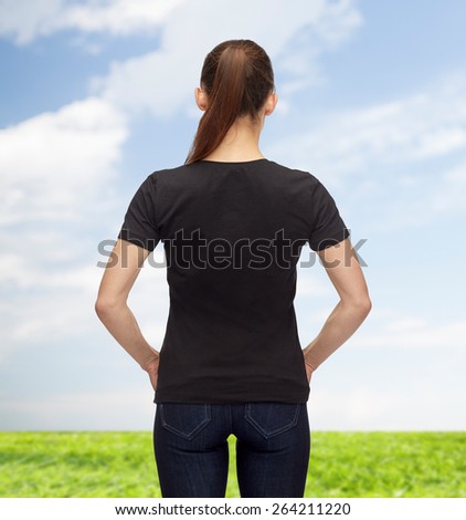 t-shirt design, advertisement and people concept - woman in blank black t-shirt from back over blue sky and grass background