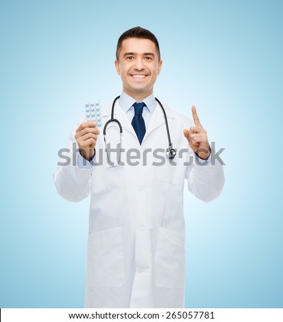healthcare, profession, people and medicine concept - smiling male doctor in white coat with tablets pointing his finger up over blue background