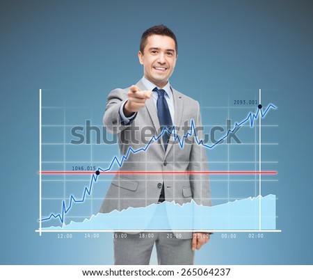 business, people and office concept - happy smiling businessman in suit pointing at you over blue background and chart
