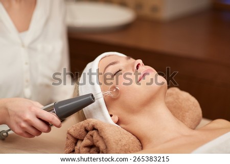 people, beauty, spa, cosmetology and technology concept - close up of beautiful young woman lying with closed eyes having face massage by massager in spa