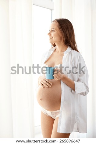 pregnancy, drinks, rest, people and expectation concept - happy pregnant woman in shirt and underware with cup drinking tea at home