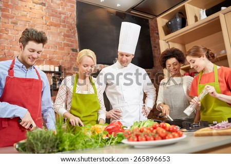 cooking class, culinary, food and people concept - happy group of friends with male chef cook cooking in kitchen