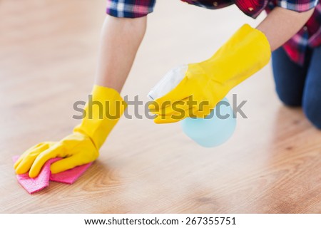 people, housework and housekeeping concept - close up of woman in rubber glover with cloth and detergent spray cleaning floor at home