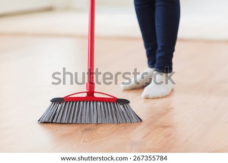 people, housework, cleaning and housekeeping concept - close up of woman legs with broom sweeping floor at home