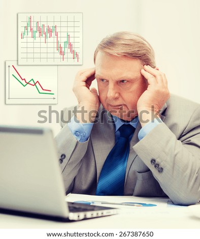 business, technology and office concept - upset older businessman with laptop and charts in office