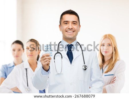 healthcare, profession, people and medicine concept - smiling male doctor in white coat with tablets over group of medics at hospital background