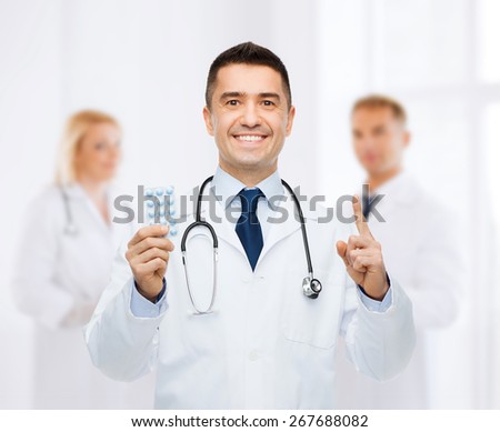 healthcare, profession, people and medicine concept - smiling male doctor in white coat with tablets pointing his finger up over group of medics at hospital background