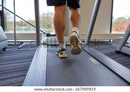 sport, fitness, lifestyle, technology and people concept - close up of man legs walking on treadmill in gym from back