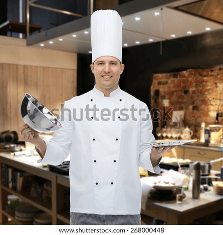 cooking, profession and people concept - happy male chef cook opening cloche cover over restaurant kitchen