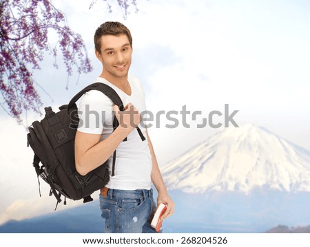 people, travel, tourism, japan and education concept - happy young man with backpack and book traveling over fuji mountain background