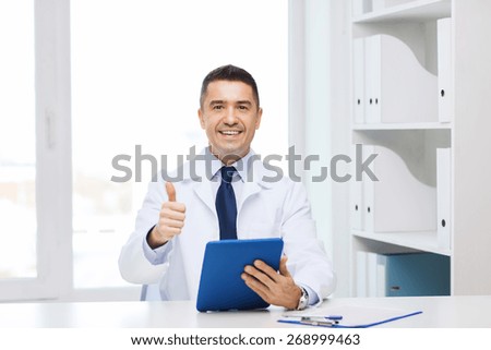 healthcare, profession, people and medicine concept - smiling male doctor in white coat with tablet pc computer showing thumbs up in medical office