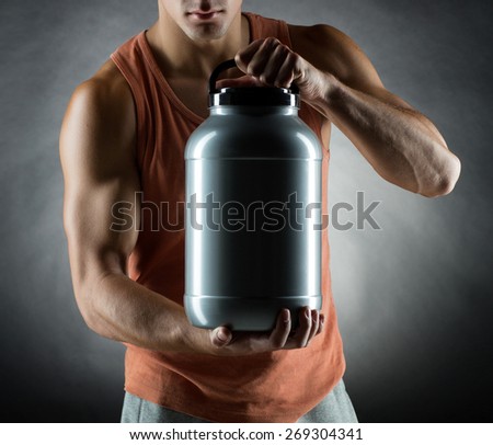 sport, bodybuilding, strength and people concept - young man standing holding jar with protein over gray background