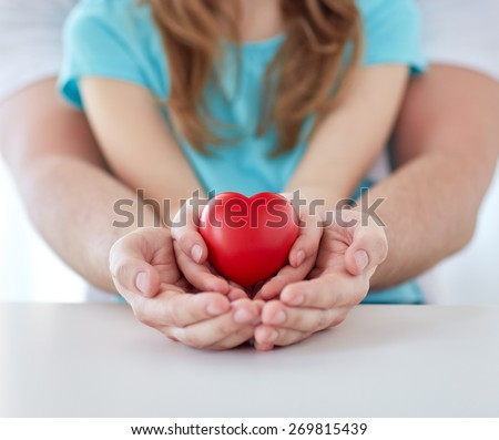 people, charity, family and advertisement concept - close up of father and girl holding red heart shape in cupped hands at home