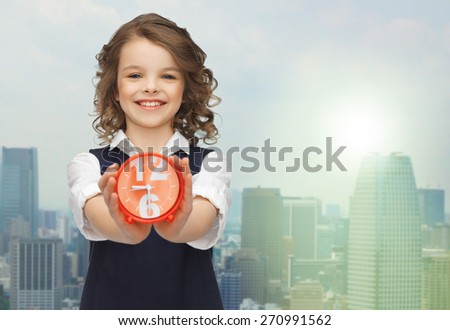 people, childhood, time and punctuality concept - happy girl with alarm clock over city background