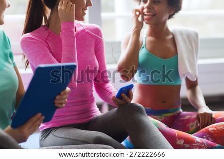 fitness, sport, technology and lifestyle concept - close up of happy women with smartphone, earphones and tablet pc computer listening to music in gym