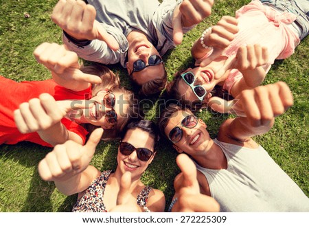friendship, leisure, summer, gesture and people concept - group of smiling friends lying on grass in circle and showing thumbs up outdoors