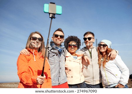 tourism, travel, people, leisure and technology concept - group of smiling teenage friends taking selfie with smartphone and monopod on city street