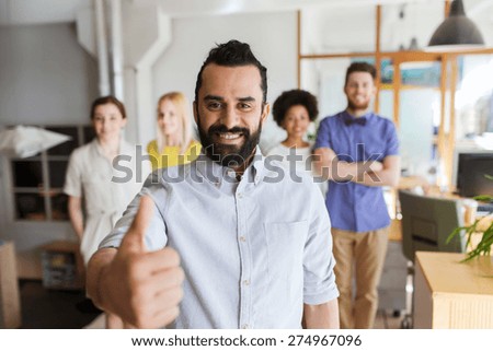 business, startup, people, success and teamwork concept - happy young man with beard over creative team showing thumbs up in office