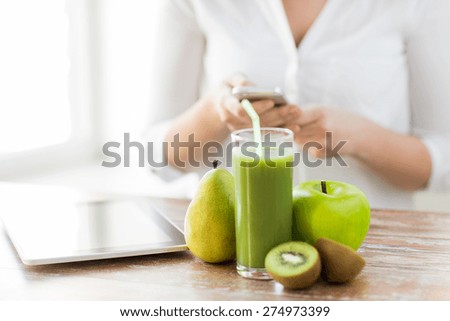 healthy eating, technology, diet and people concept - close up of woman hands holding smartphone with tablet pc, fruits and fresh juice sitting at table