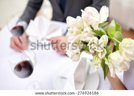 restaurant, people, celebration and holiday concept - close up of young couple with tulip flowers and glasses of red wine at restaurant