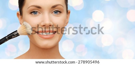 beauty, people, holidays  and makeup concept - happy woman face applying powder foundation with brush over blue lights background
