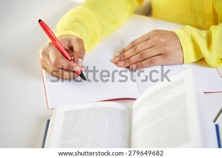 people and education concept - close up of fafrican american female hands with book writing to notebook at school