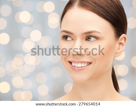 health, people and beauty concept - beautiful young woman face over holidays lights background