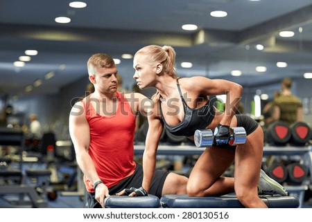 fitness, sport, exercising, bodybuilding and weightlifting concept - young woman and personal trainer with dumbbells flexing muscles in gym