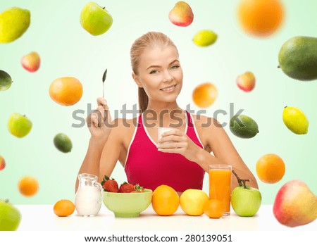 healthy eating, diet, organic food and people concept - happy woman eating yogurt and having breakfast over green background with falling fruits