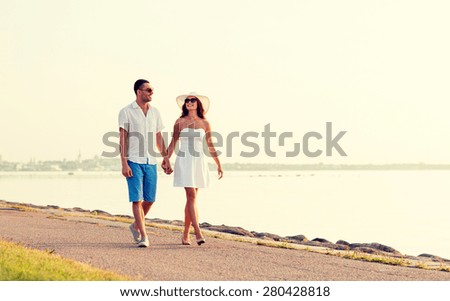 love, travel, tourism, summer and people concept - smiling couple on vacation wearing sunglasses and holding hands walking at seaside