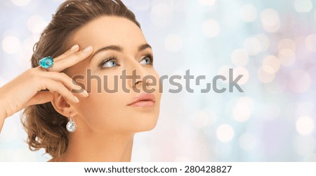 beauty, jewelry, people and accessories concept - close up of woman face with cocktail ring on hand and earrings over blue holidays lights background