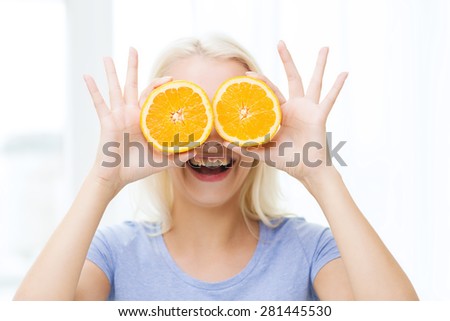 healthy eating, organic food, fruit diet, comic and people concept - happy woman having fun and covering her eyes with orange slices