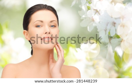beauty, people and health concept - beautiful young woman touching her face over green blooming garden background