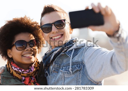 friendship, relations, tourism, travel and people concept - happy teenage friends or couple in sunglasses with smartphone taking selfie outdoors